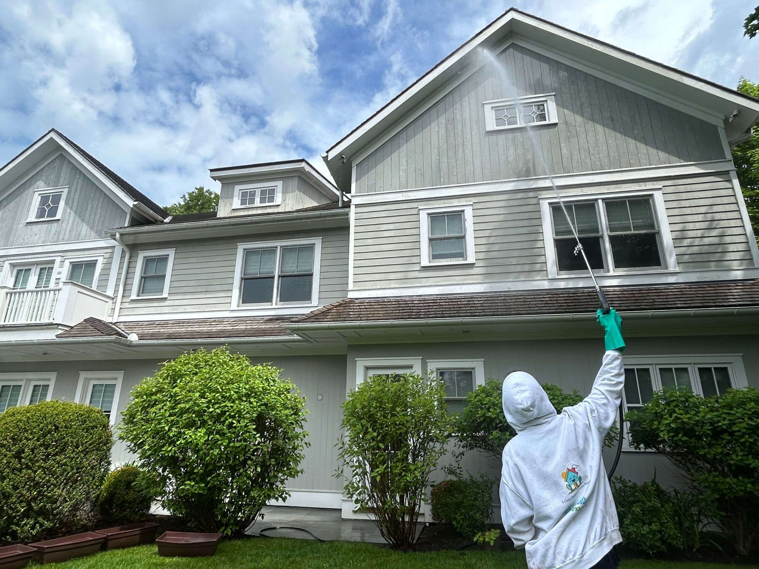 House Bath technician washing the upper siding of a large gray home